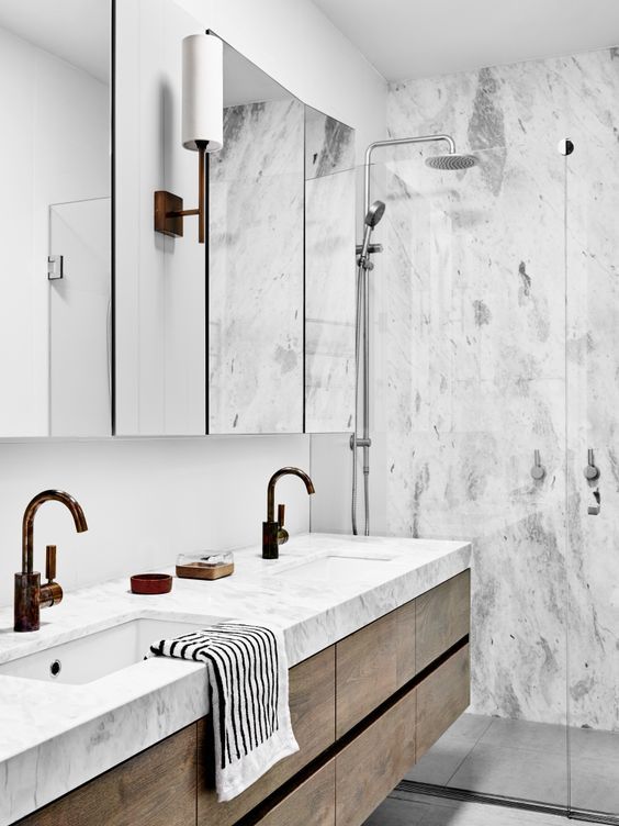 Another beautiful and simple bathroom, with what appears to be gorgeous large-format tile is kept open and simple by a glass divider at the end of the double vanity.