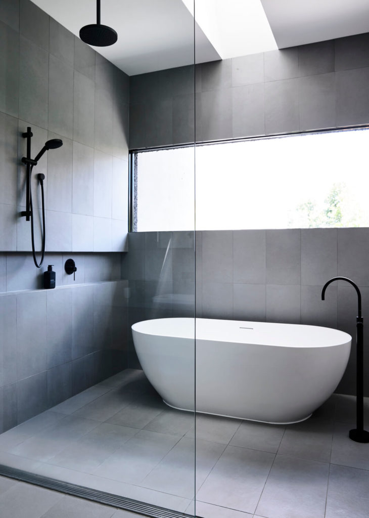 The Hawthorn House by Domoney Architecture and Heartly uses a calming neutral palette throughout the house and continues it into the bathroom. Using swaths of cool dark tile and concrete floors against the Australian daylight, the bathroom skylight design echoes the tranquility of the rest of the home.